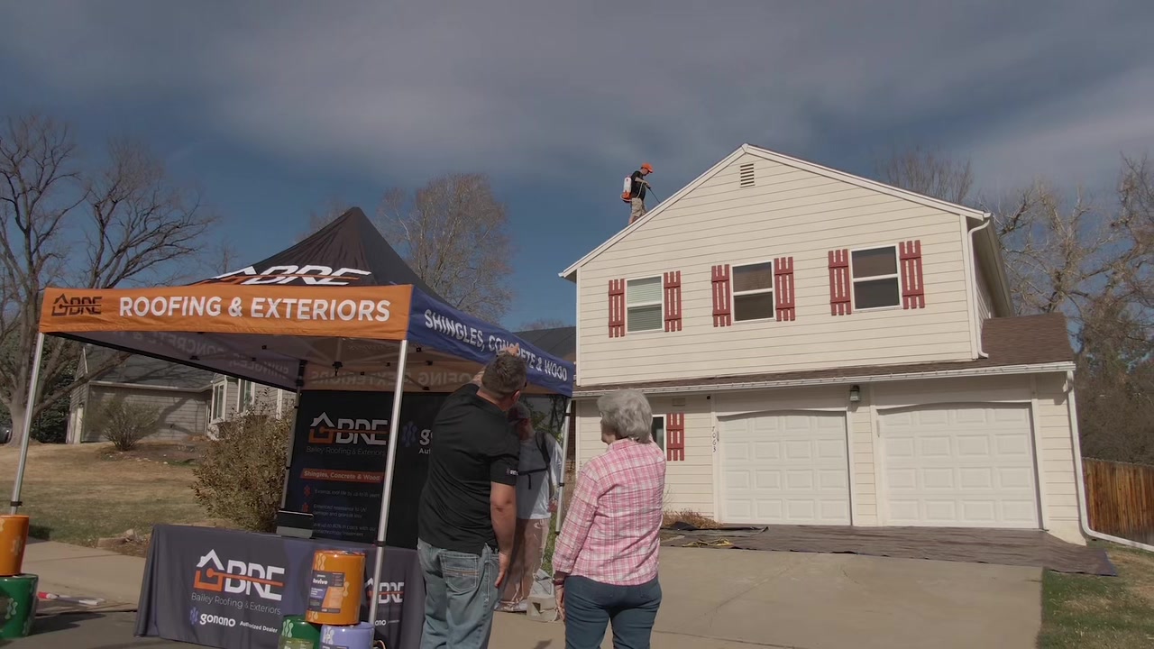 Bailey Roofing GoNano application day — crew member spraying the roof while homeowners visit the BRE tent below, June 2026