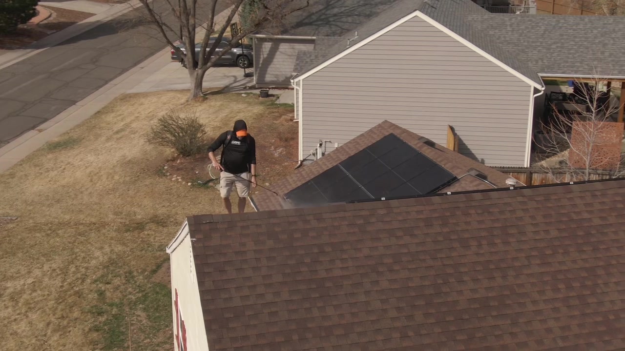 Bailey Roofing crew member applying GoNano coating with a backpack sprayer beside solar panels on a Front Range roof, June 2026