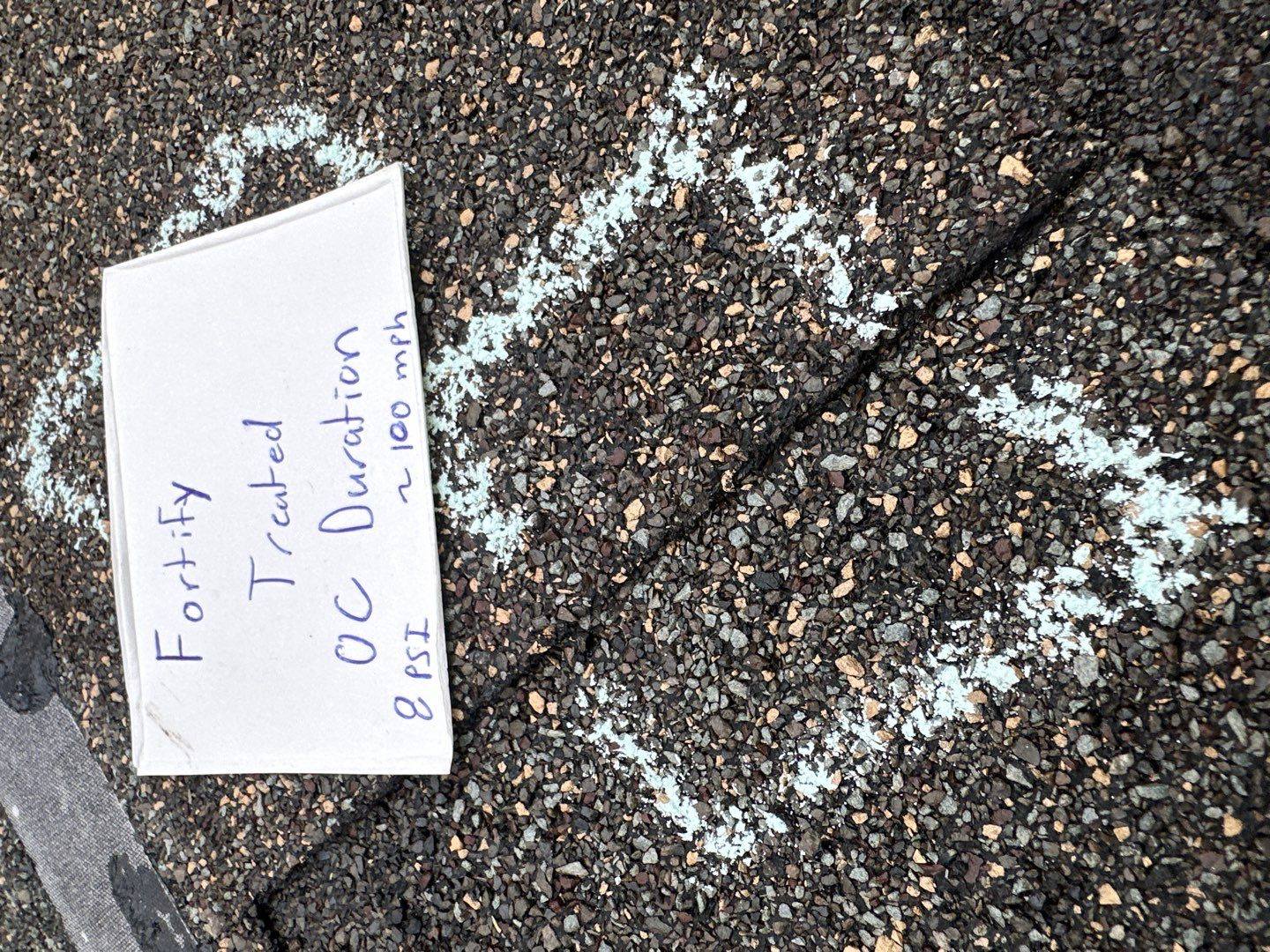 NuRoof Fortify treated Owens Corning Duration shingle with chalked hit zone and labeled test card, intact after roughly 100 mph simulated hail in Bailey Roofing's bench test, April 2026