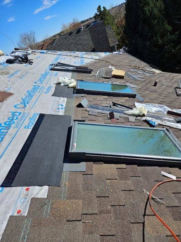 New skylights flashed into place mid-reroof by Bailey Roofing on East Powers Drive in Piney Creek, Centennial, shingles fitted around the curbs over CertainTeed RoofRunner underlayment, March 2024